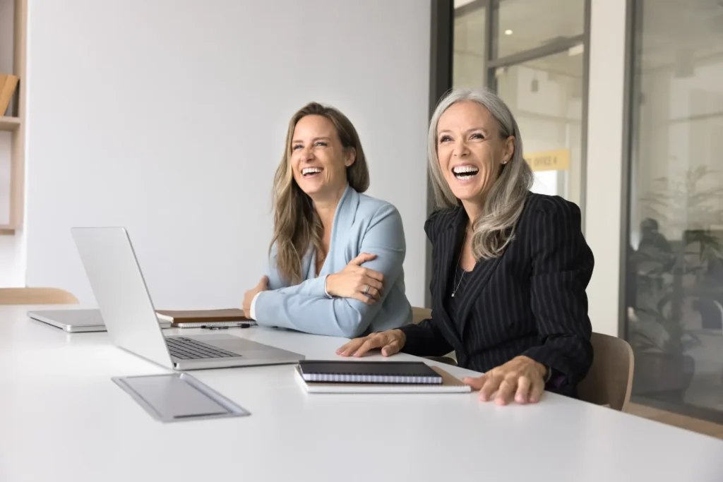 Two women smiling and conversing in a professional office setting.