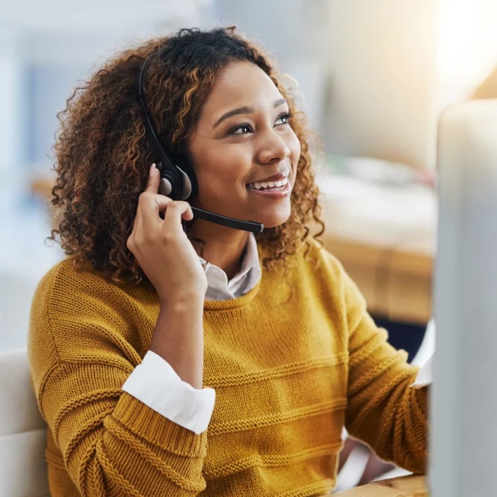 Professional woman wearing a headset, smiling while engaged in a client phone call.
